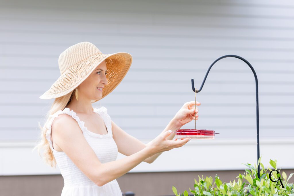 A woman holding a hummingbird feeder with homemade hummingbird food in her garden.
