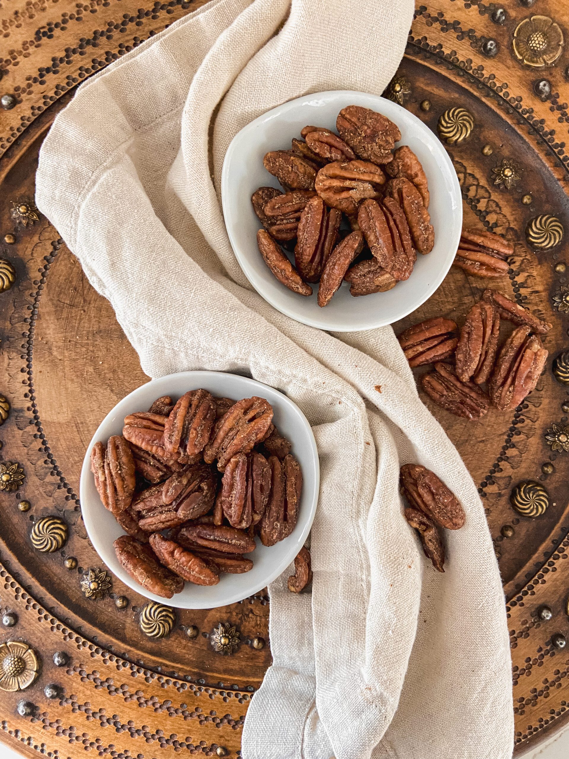 Two white bowls with candied pecans on a wooden bread board.