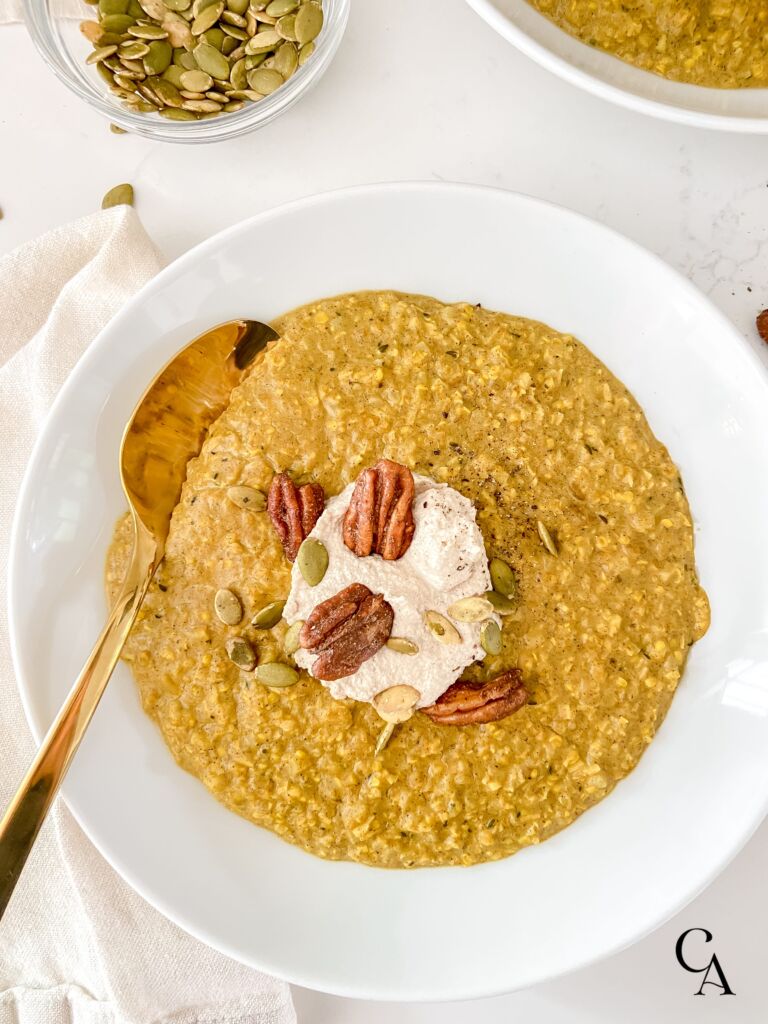 Chai spiced golden oatmeal in a white bowl, topped with pecans and cashew cream.