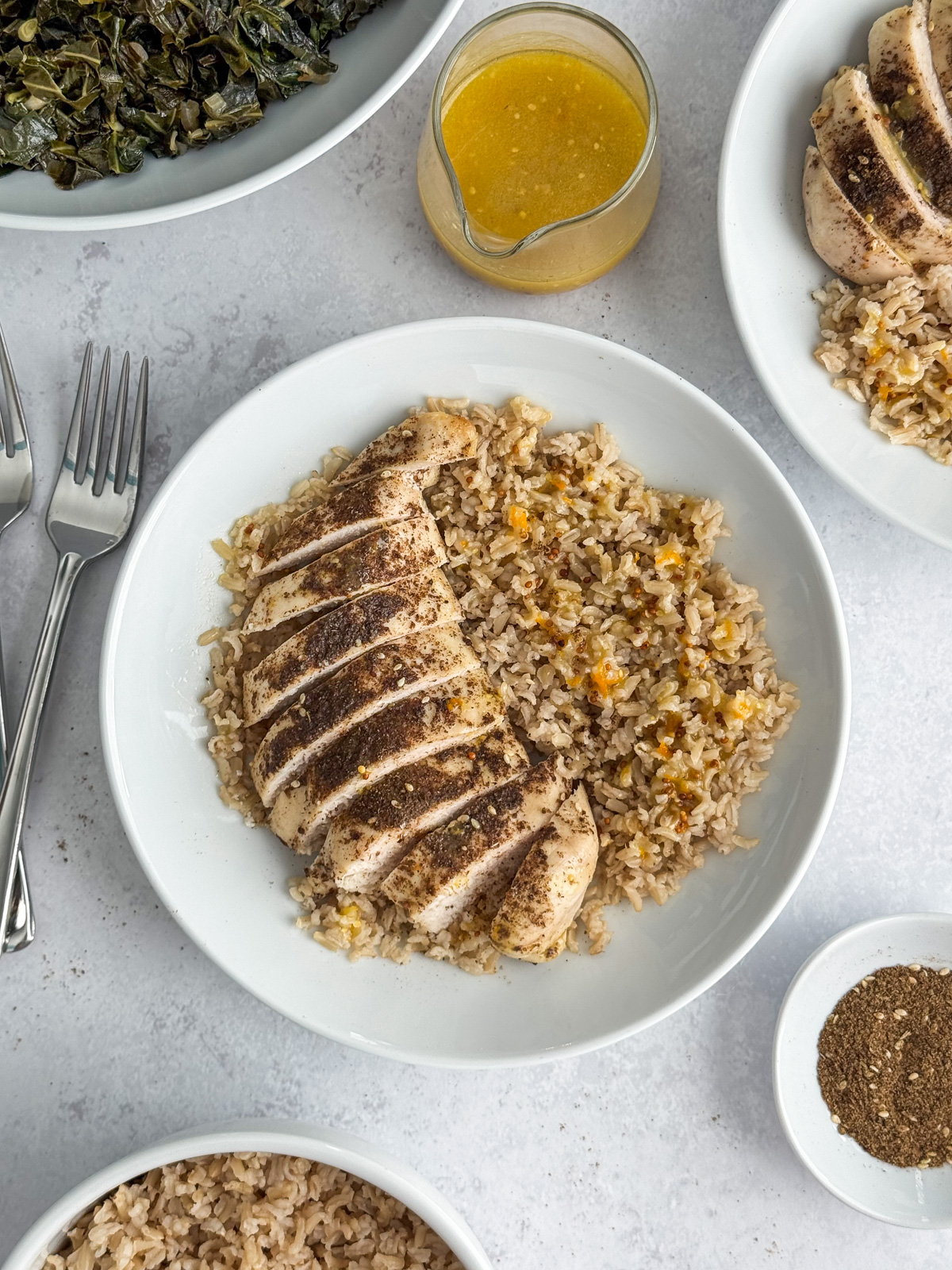 A plate of brown rice with a sliced za'atar chicken breast next to a sauce.