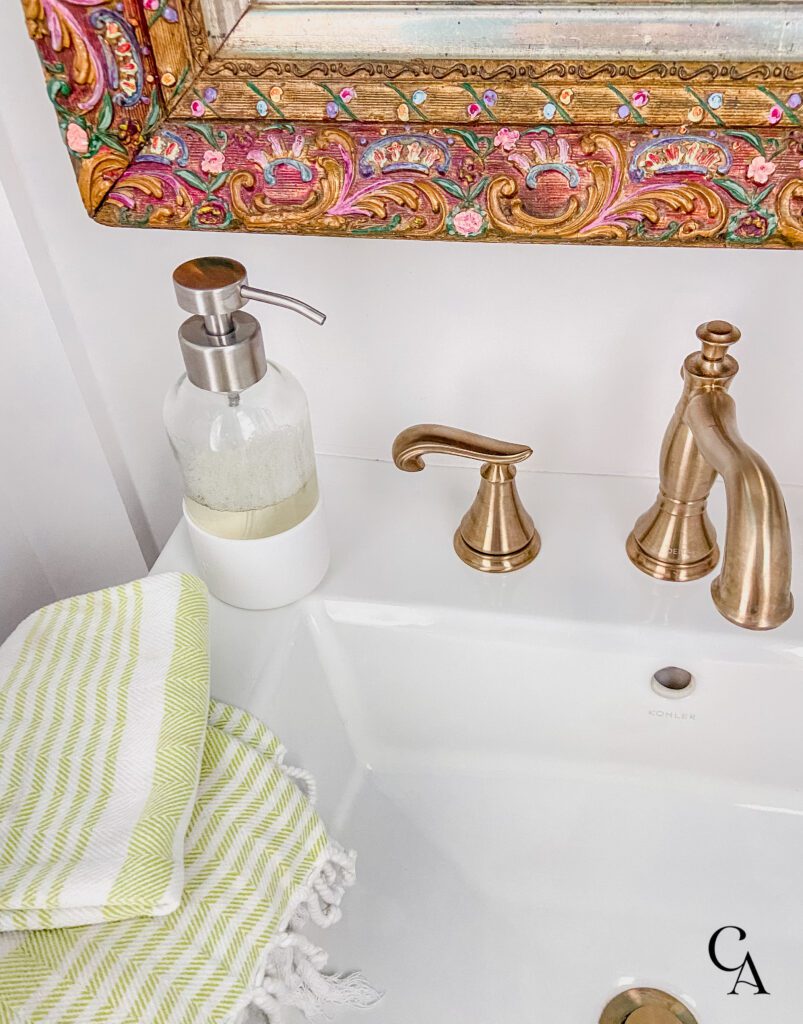 Glass bottle of Branch Basics hand soap on a white sink with a gold faucet.
