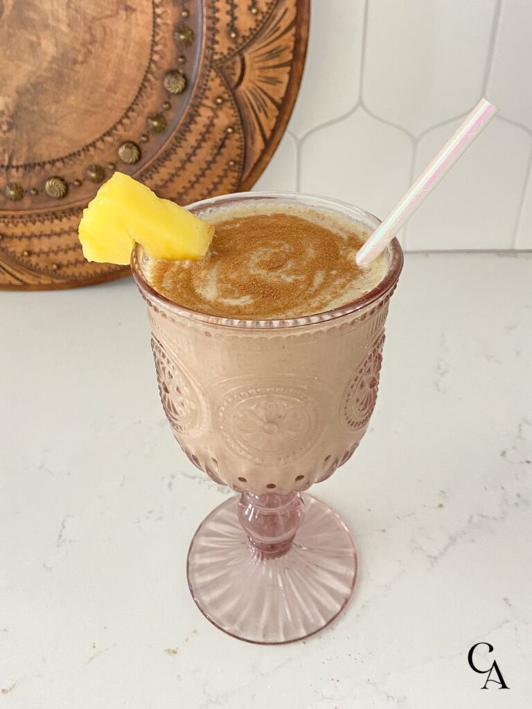 A piña colada smoothie in a pink goblet with a slice of pineapple.