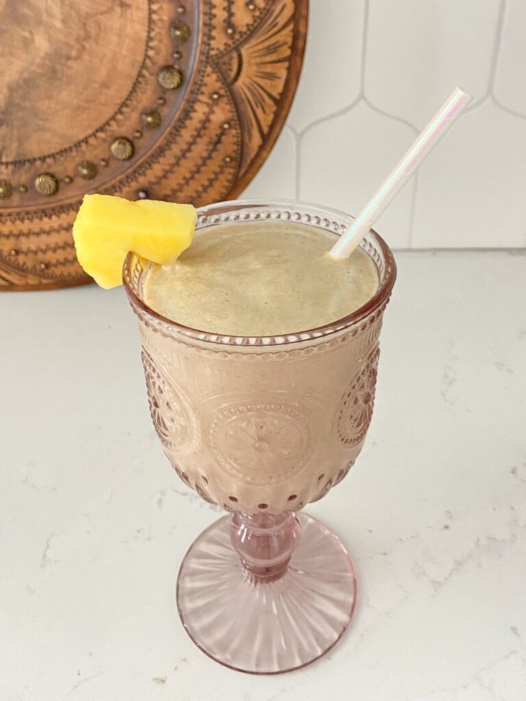 A pink glass with a piña colada smoothie and straw.