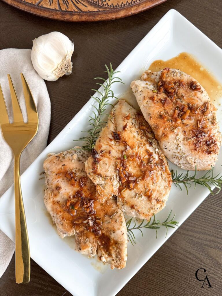 Rosemary garlic chicken breasts on a white serving plate on top of a wood table.