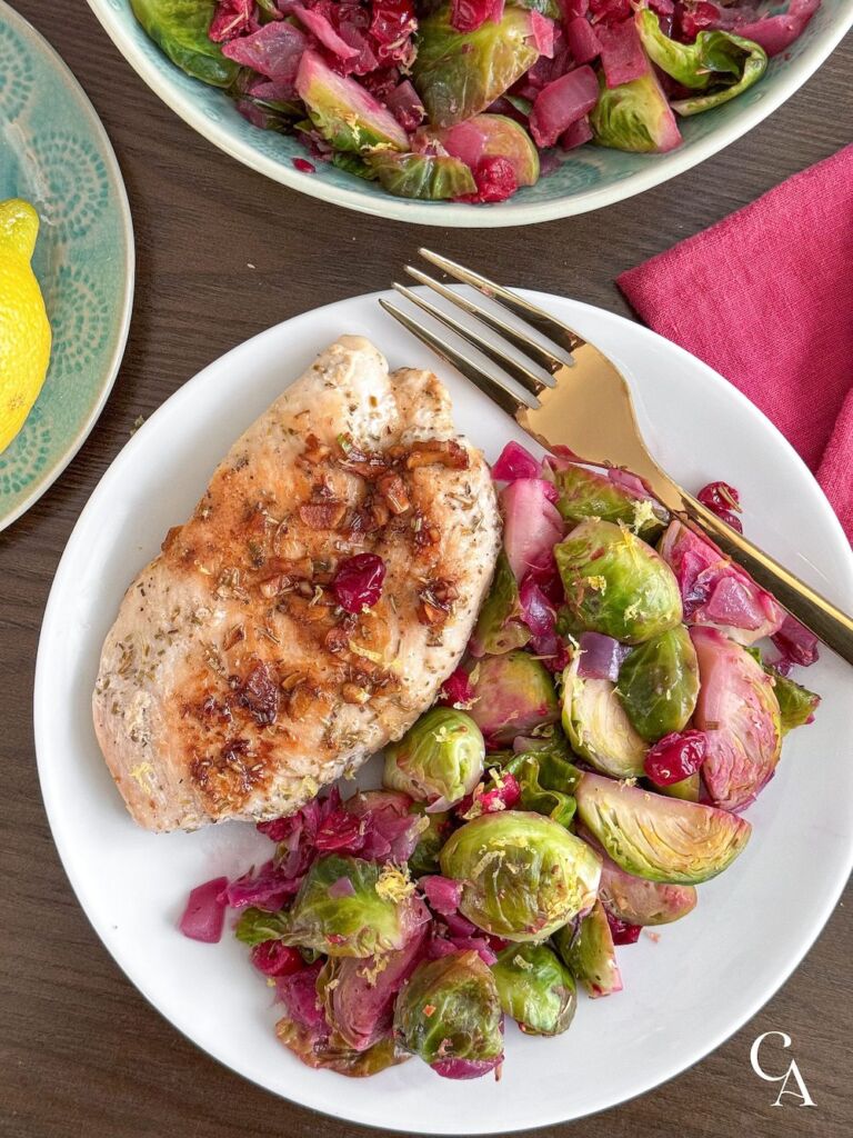 A white plate with a chicken breast and veggies on the side.