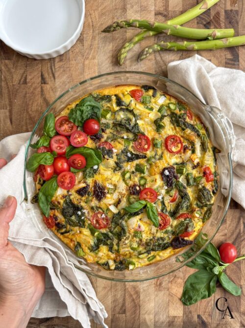 An asparagus frittata with tomatoes and basil leaves on top.