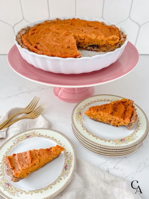A sweet potato tart on a pink cake stand with slices on plates below.