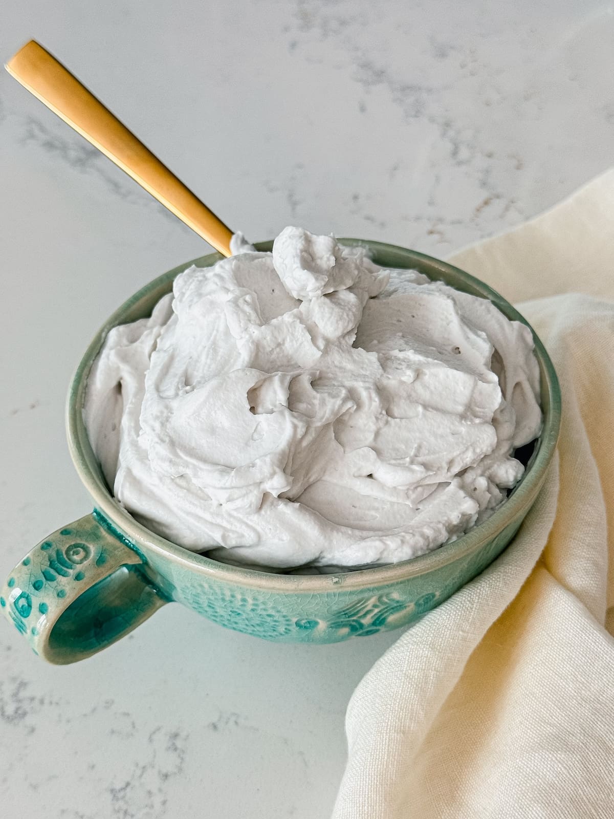 A bowl of coconut whipped cream with a gold spoon.