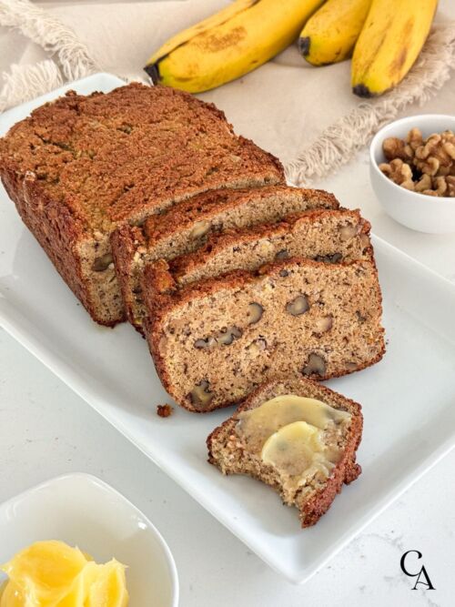 Sliced almond flour banana bread on a white plate with ghee spread.