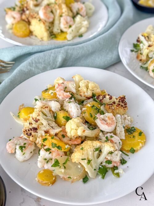 A white plate of cooked vegetables and shrimp.