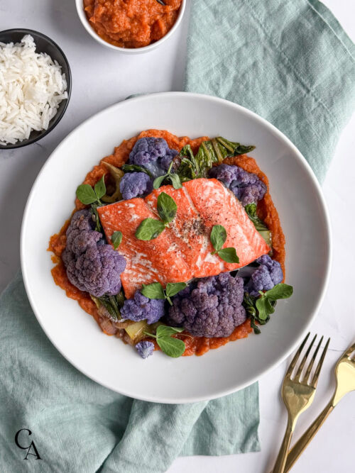 Seared salmon filets with colorful veggies in white bowls on a marble counter.