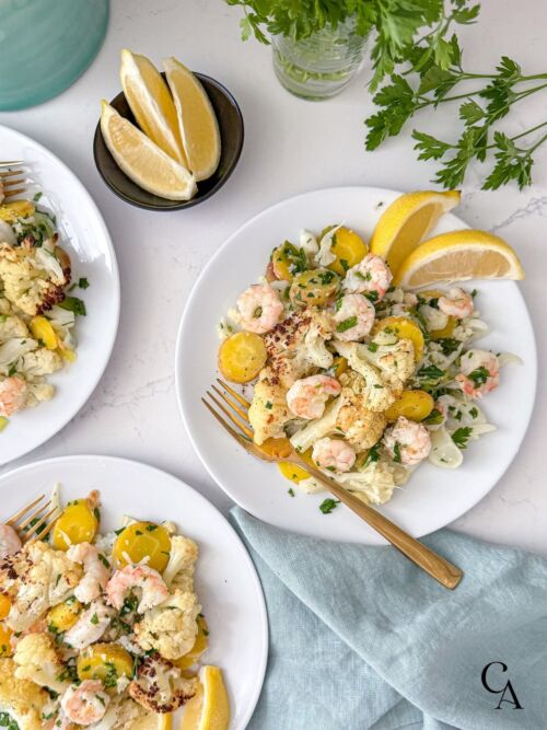 Plates of veggies and shrimp with lemon wedges and forks on a counter.