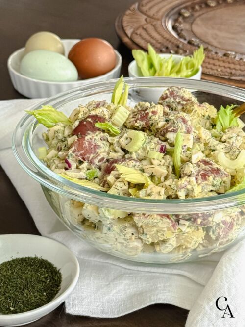 A serving bowl of new potato salad with dill and hard-boiled eggs.