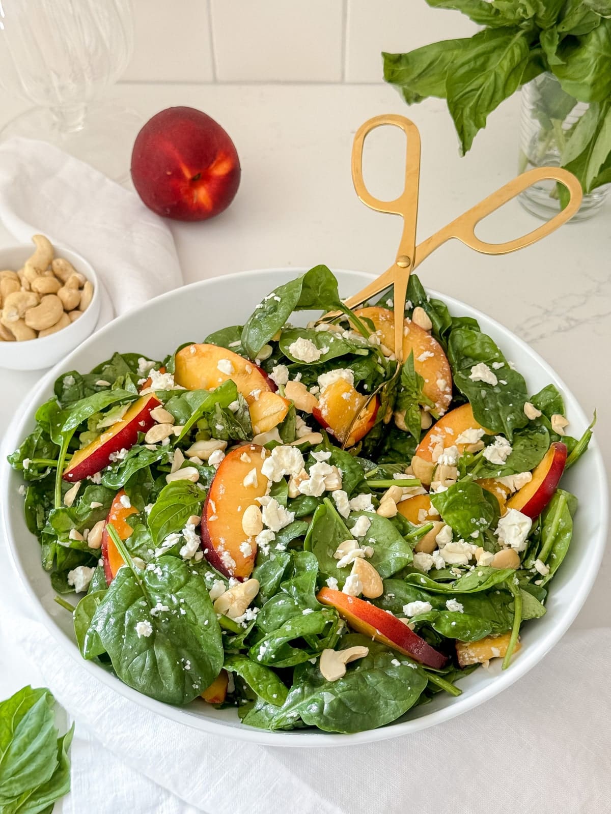A spinach and nectarine salad in a large bowl with gold tongs.
