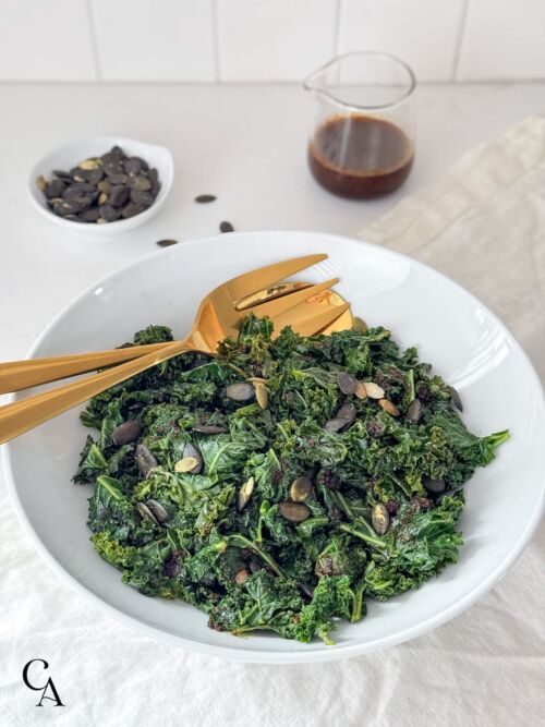 A bowl of steamed kale with pumpkin seeds and brown sauce.