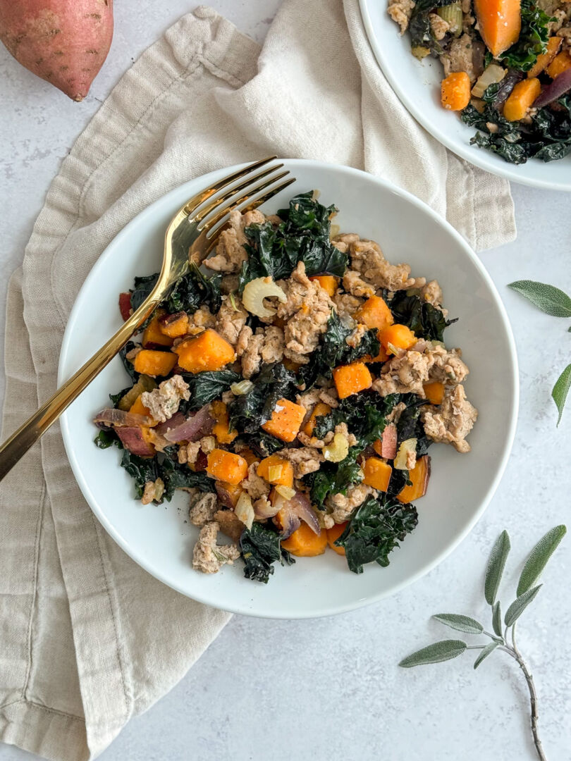 A bowl of ground turkey, chopped sweet potatoes and kale wit a gold fork resting inside.