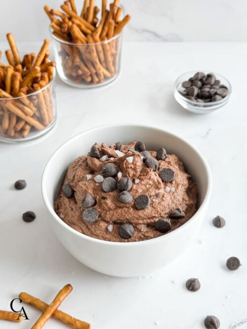 A bowl of chocolate fruit dip with pretzel sticks.