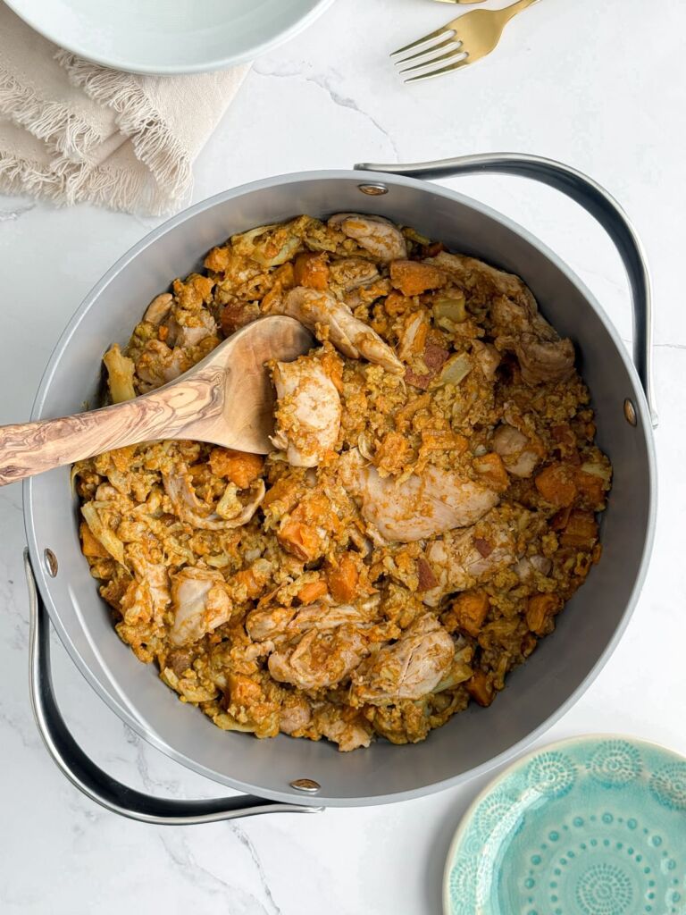 A pot of chicken vindaloo with sweet potatoes and cauliflower florets on a marble counter.
