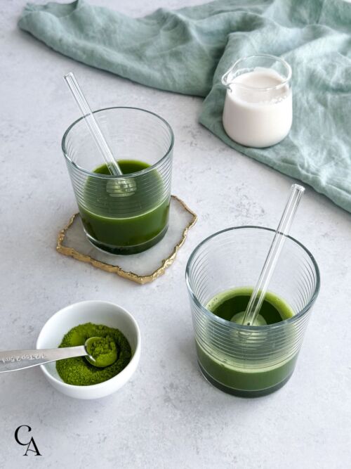 Two glasses of a green drink next to a bowl of matcha green tea powder.