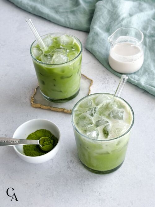 Two green, creamy drinks and a bowl of matcha powder.