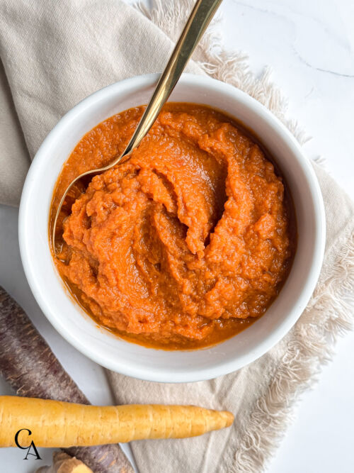 A bowl of carrot dip with ginger and coconut aminos next to whole carrots.
