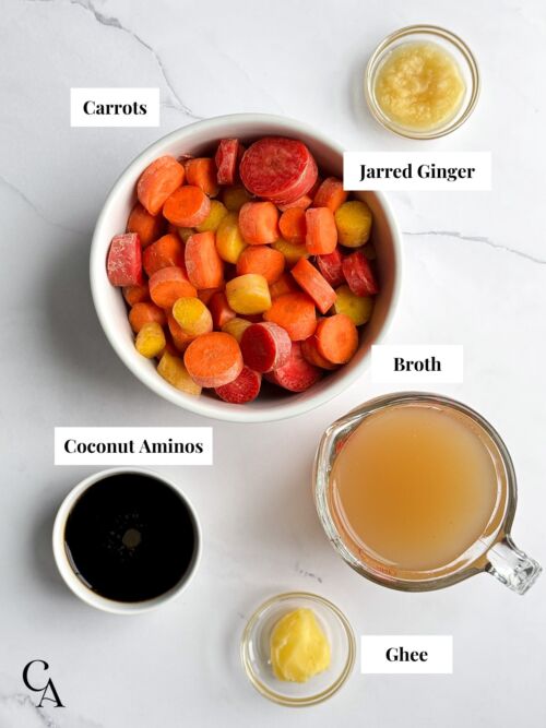 Bowls of sliced carrots, minced ginger, coconut aminos, ghee, and chicken broth on a marble counter.