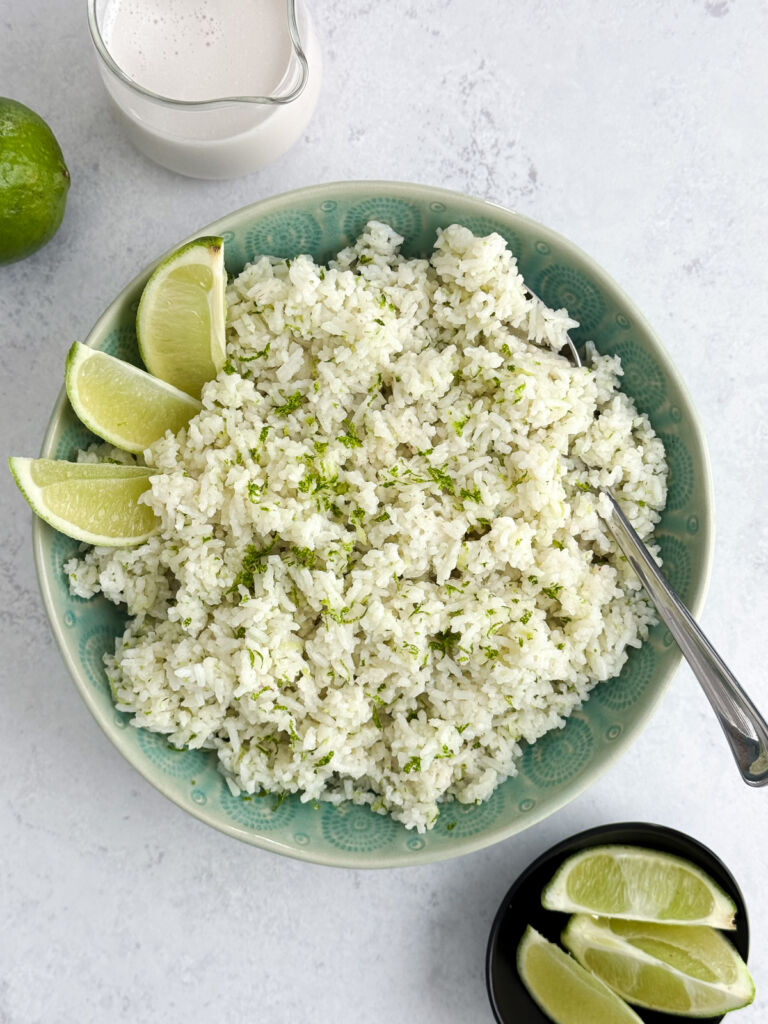 A turquoise bowl of coconut lime rice with lime wedges on the side.