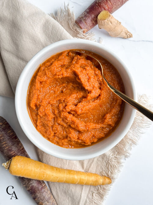 Puréed carrots in a white bowl with a gold spoon.