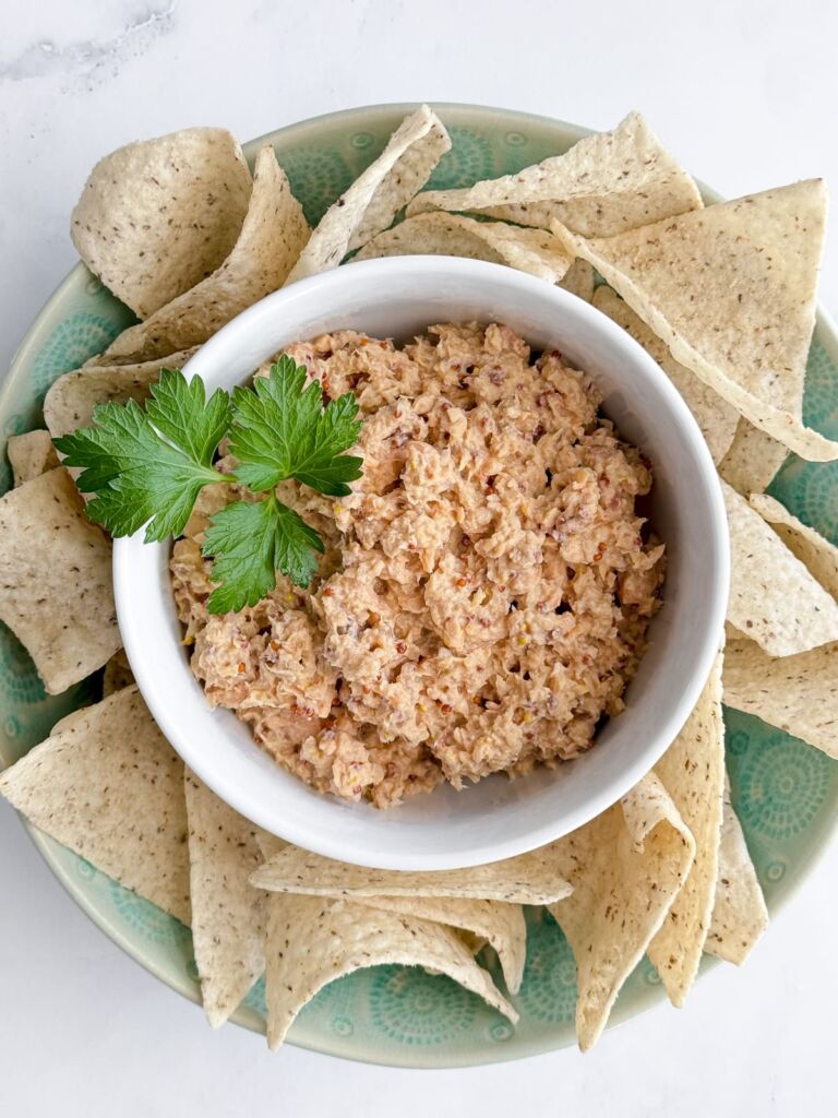 A bowl of salmon dip garnished with fresh parsley leaves and tortilla chips on the side.