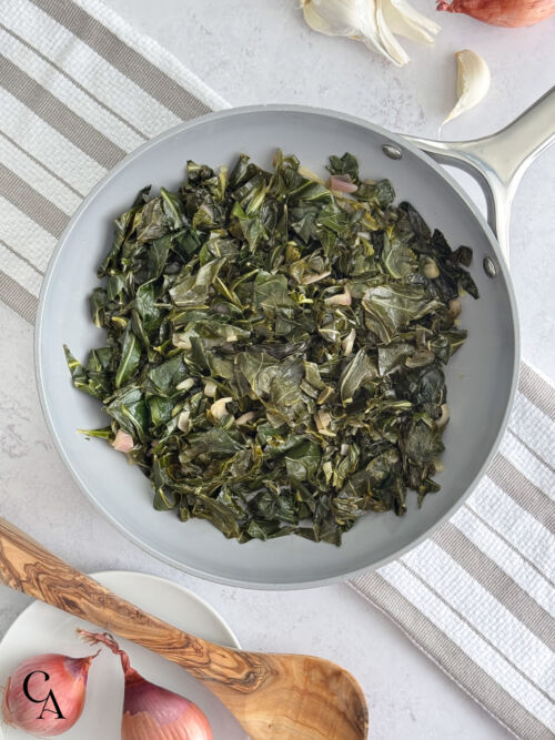 Rustic, sautéed collards in a pan with shallots, a head of garlic and a wooden spoon.
