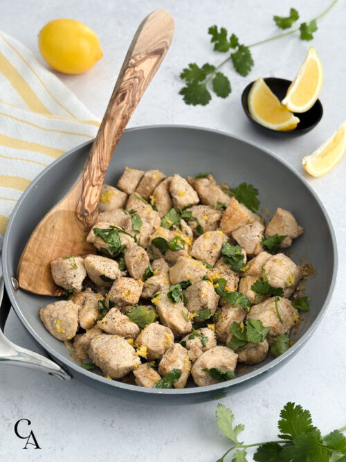 A pan of coriander chicken garnished with cilantro, lemon zest and black pepper.