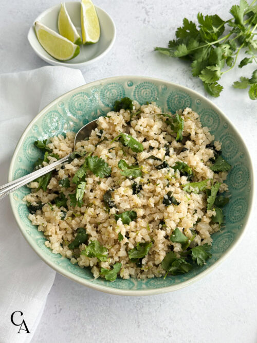 A bowl of cilantro lime cauliflower rice with a silver spoon.