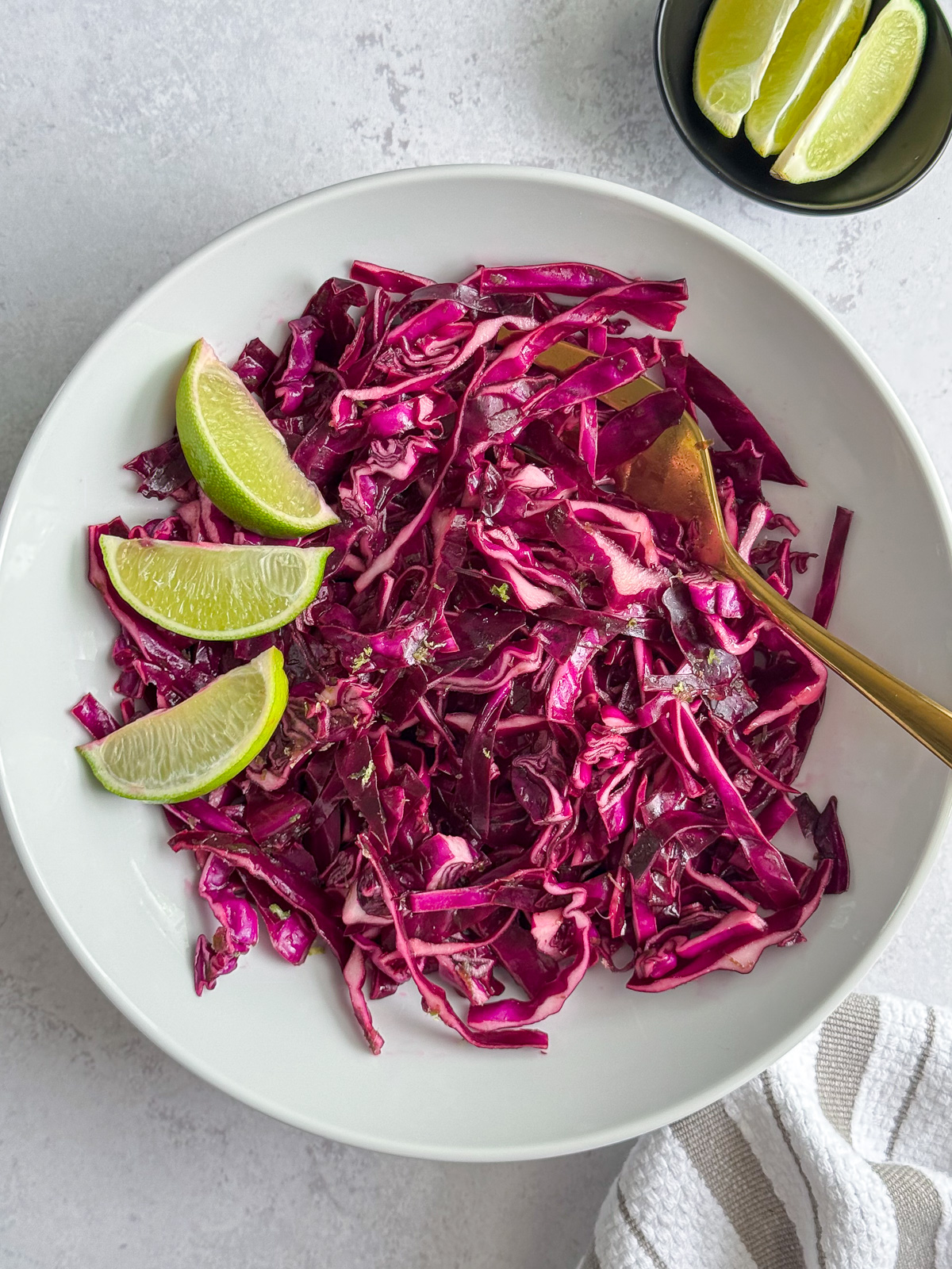 A bowl of coleslaw with cabbage and fresh limes.