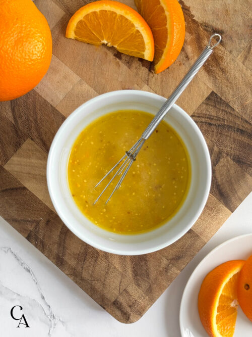 A bowl of sweet vinaigrette on a wooden surface, with sliced oranges on the side.
