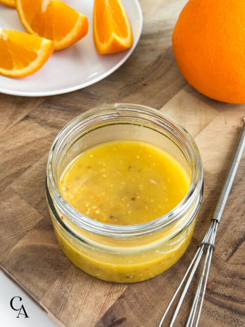 A glass jar of a simple vinaigrette made with orange juice, zest, and whole grain mustard.