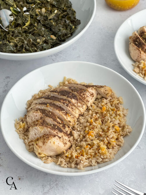 Sliced za'atar chicken breasts over rice, with a bowl of greens in the background.