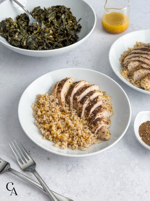 A plate of basmati rice with sliced chicken sprinkled with seasoning and a bowl of collards.