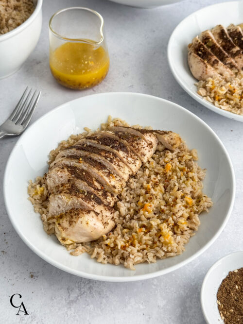 A chicken and rice bowl with a jar of sauce in the background.