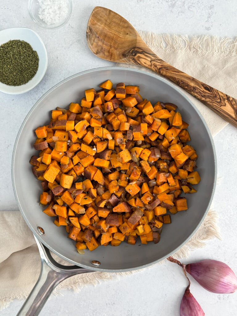 A pan of diced orange sweet potatoes with an olive wood spoon and a bowl of flaky salt.