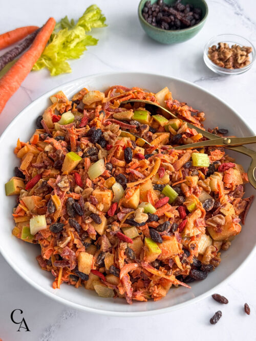 Close up of a shredded carrot raisin salad with chopped fruits and nuts.