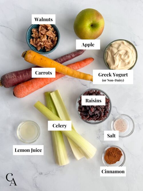 A tablescape of ingredients for making carrot raisin salad with apples and Greek Yogurt.