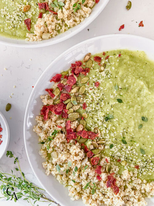 An overhead shot of bowls of broccoli cauliflower soup topped with millet, fresh thyme and turkey bacon.