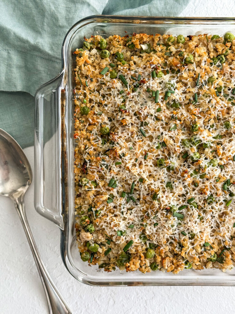 Overhead shot of a salmon casserole sprinkled with melted shredded cheese and fresh chives, with a spoon and a linen napkin next to it.