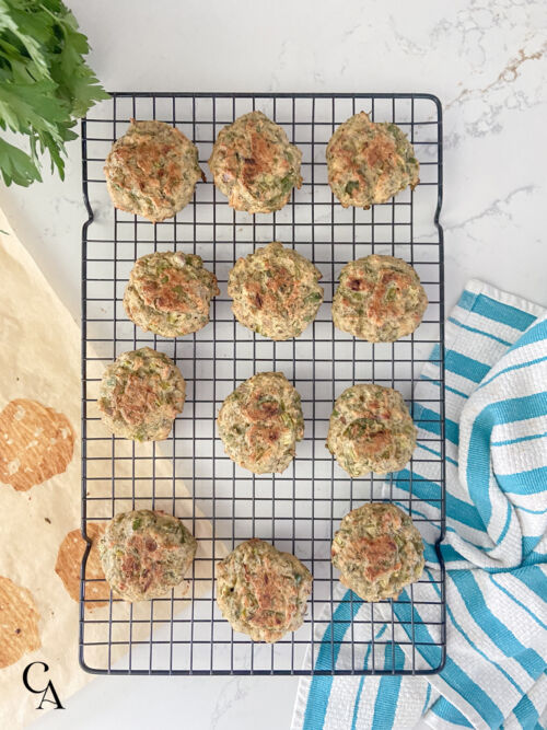 12 salmon patties on a black wire cooling rack next to a striped towel and a bunch of parsley.