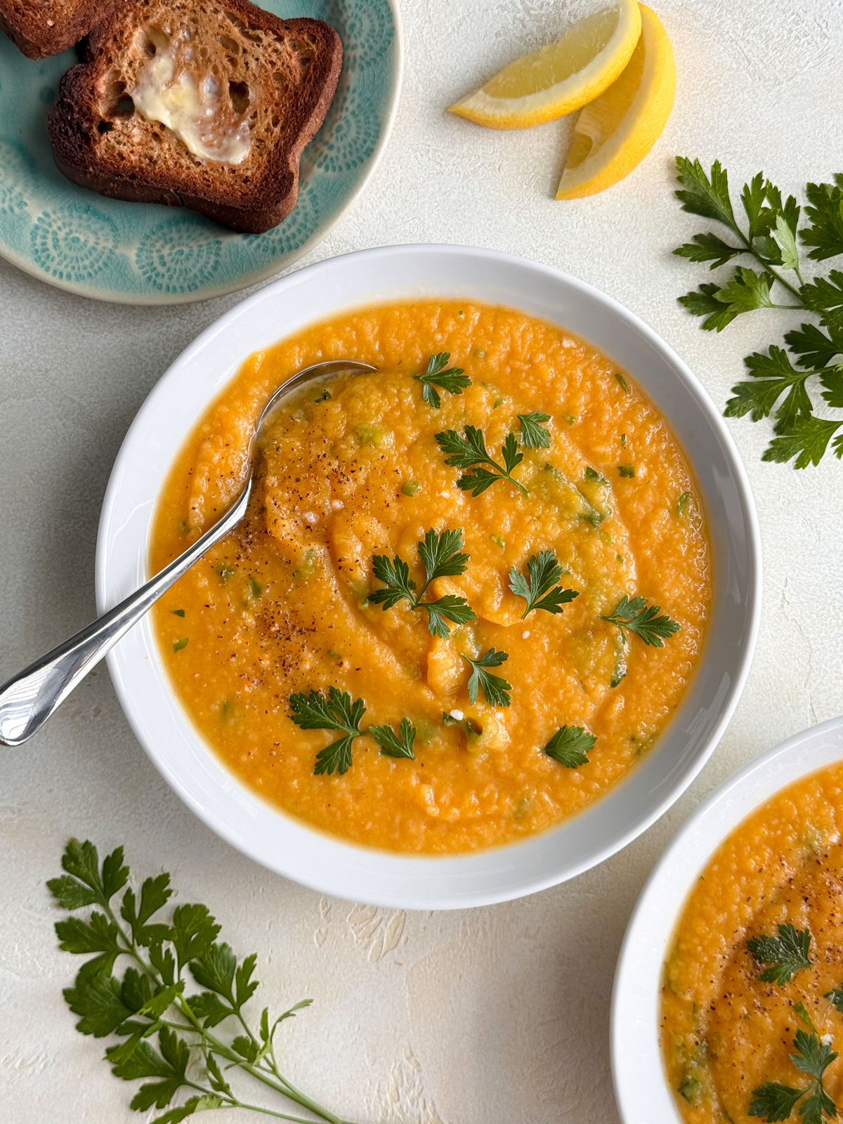 Bowl of creamy roasted butternut squash soup garnished with fresh parsley, served with crusty toast and lemon wedges on the side.