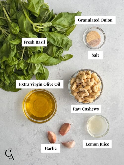 Bowls of ingredients on a counter, including raw cashews, olive oil, salt, and fresh basil.