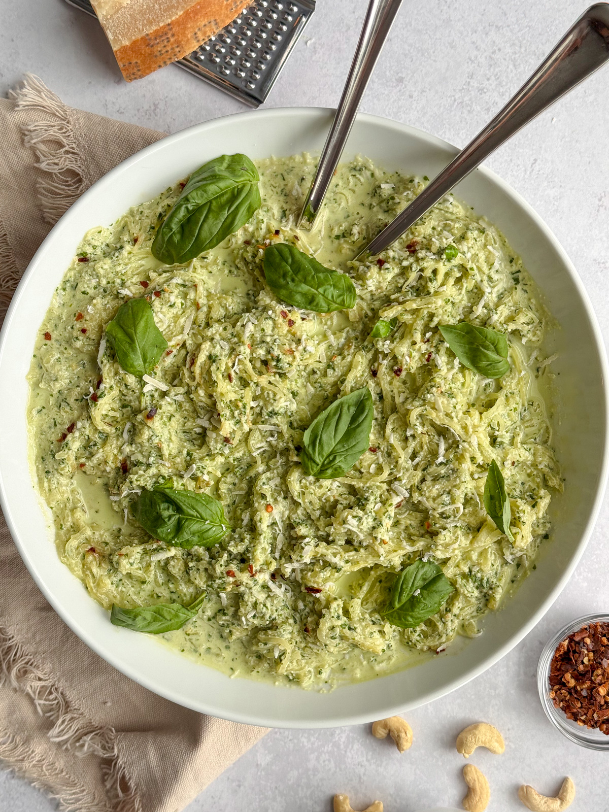 Creamy pesto spaghetti squash in a white bowl, garnished with fresh basil and red pepper flakes, served with two forks for sharing.
