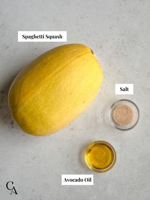 A spaghetti squash with pinch bowls of salt and avocado oil on a light gray surface.