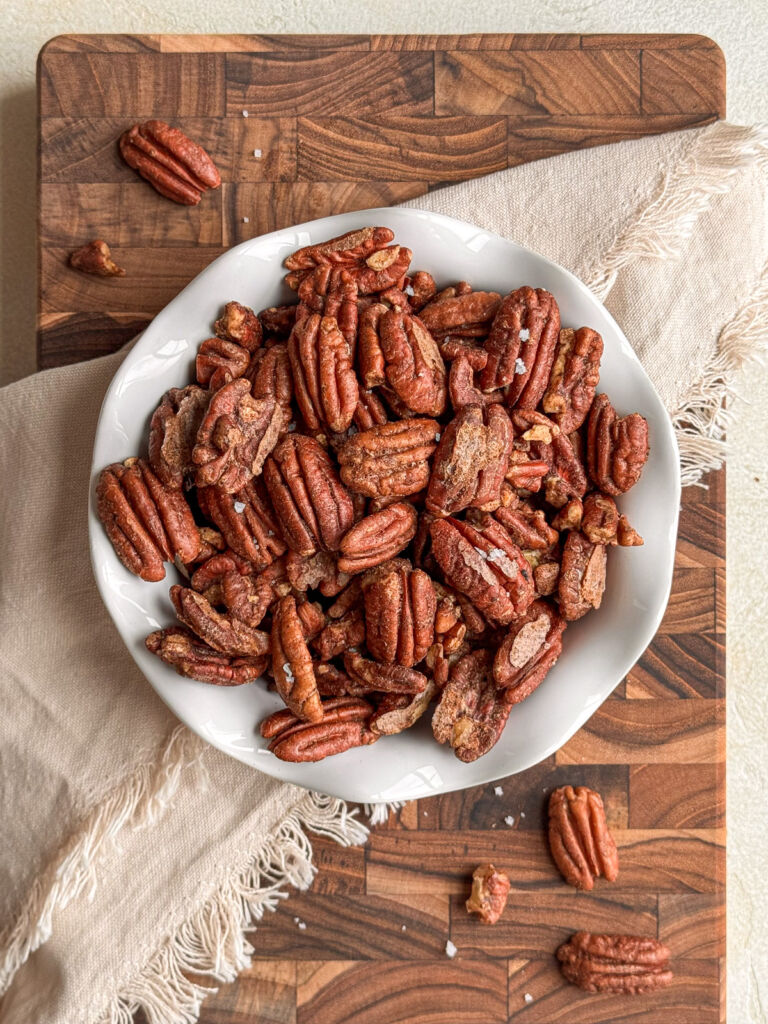 A bowl of pumpkin-spiced candied pecans sprinkled with fleur de sel, on top of a cutting board.