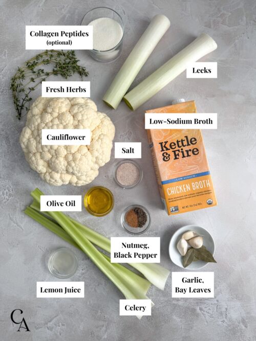 Flat lay of labeled soup ingredients, including cauliflower, leeks, celery, garlic, olive oil, broth, salt, lemon juice, spices, and fresh herbs.